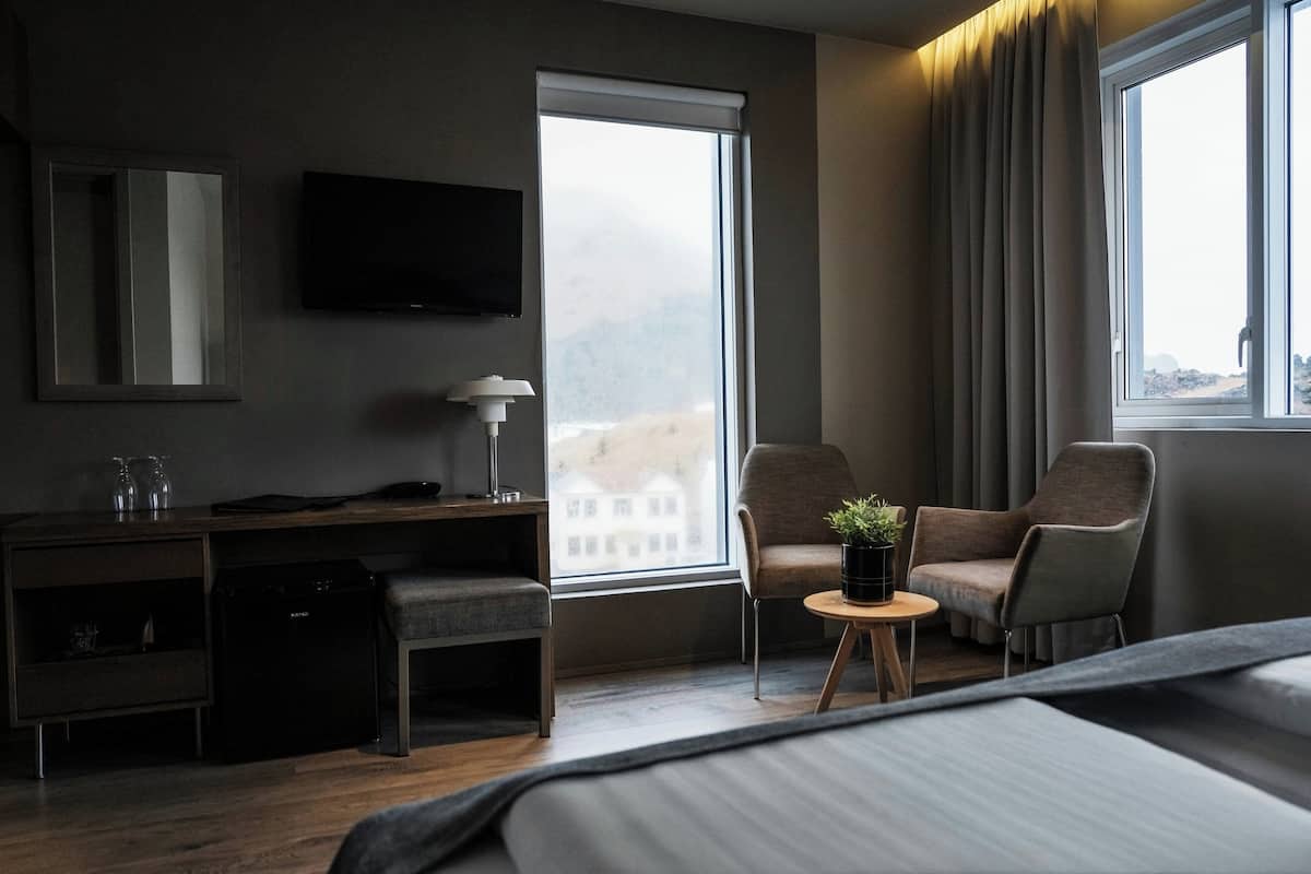 Ein Hotelzimmer mit Bett, Schreibtisch, Stuhl, Fernseher und einem Fenster mit Vorhängen.