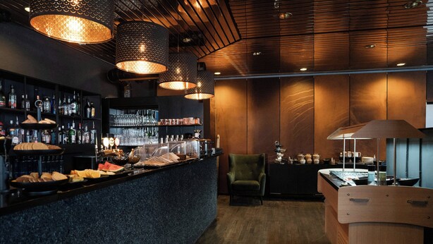 A bar area with a counter, shelves of bottles, and hanging lights.