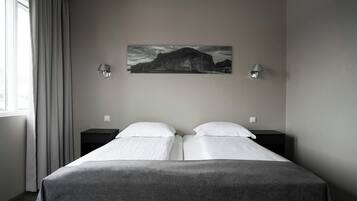 Habitación de hotel con una cama, dos mesitas de noche, una lámpara de pared y un cuadro de un paisaje montañoso.