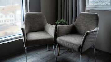 Dos sillones grises con patas de metal en una habitación con un ventanal grande, una planta y vistas a un edificio.