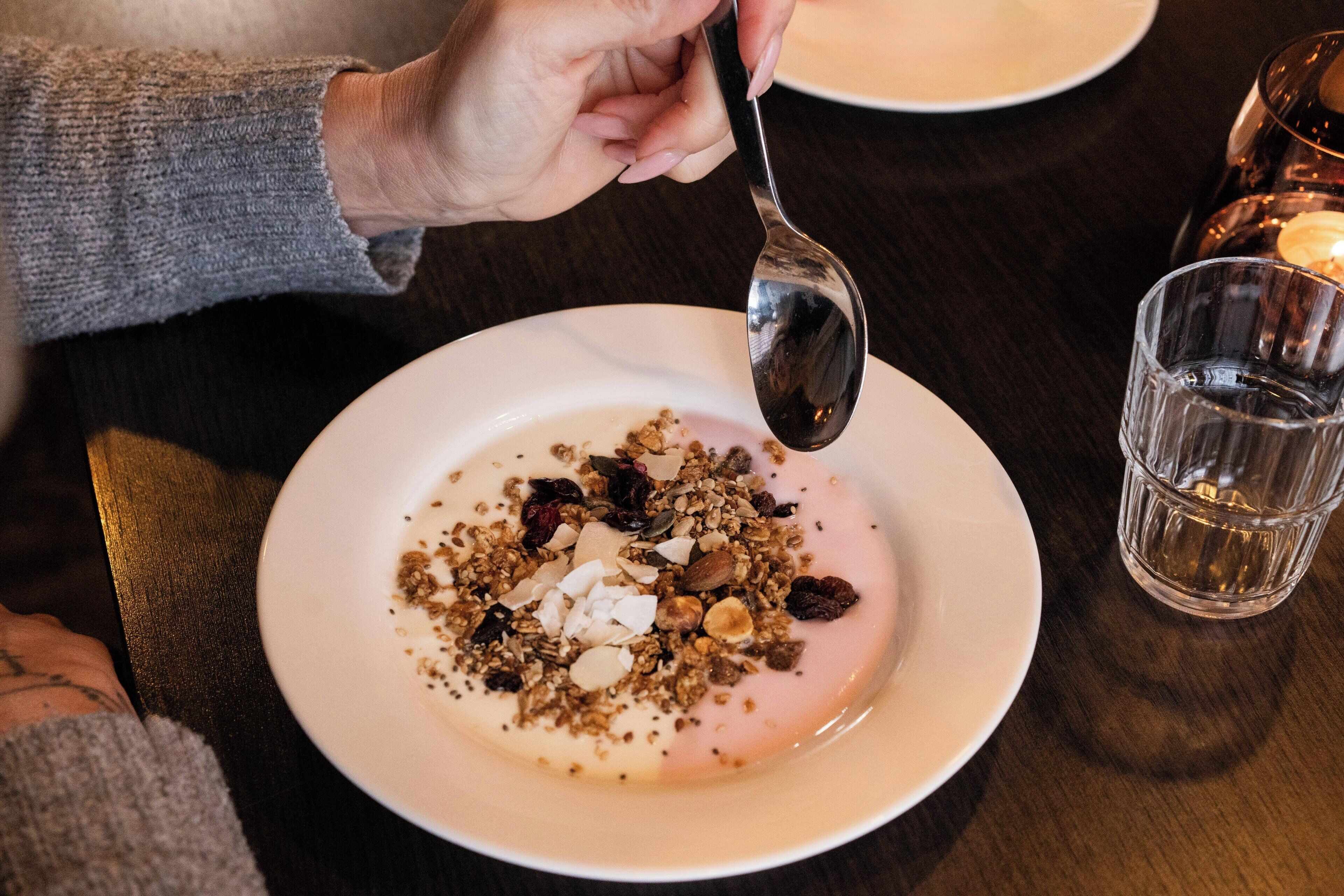 Primer plano de un postre con granola y nueces sobre un plato blanco, con una cuchara cerca.
