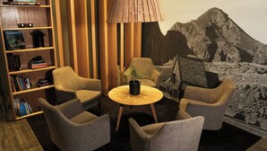 A room with a bookshelf, two armchairs, a round table with a plant, and a large wall mural of a mountain.