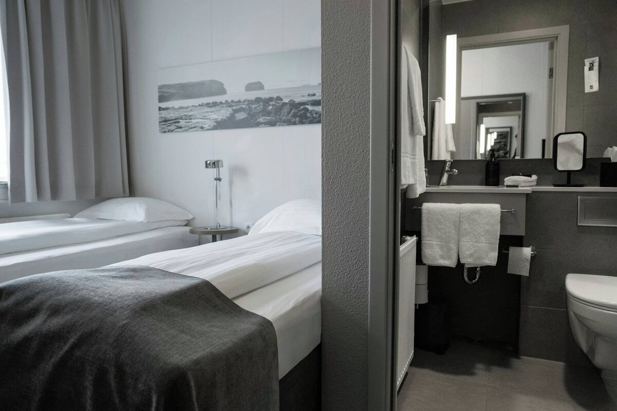 A hotel room with two beds, a bathroom, and a view of the sea.