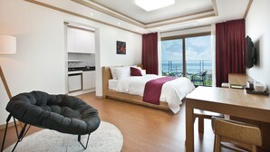 A modern hotel room with a bed, a desk, a chair, a kitchen area, and a balcony with a view. - Familia Hotel Jeju (Seogwipo)