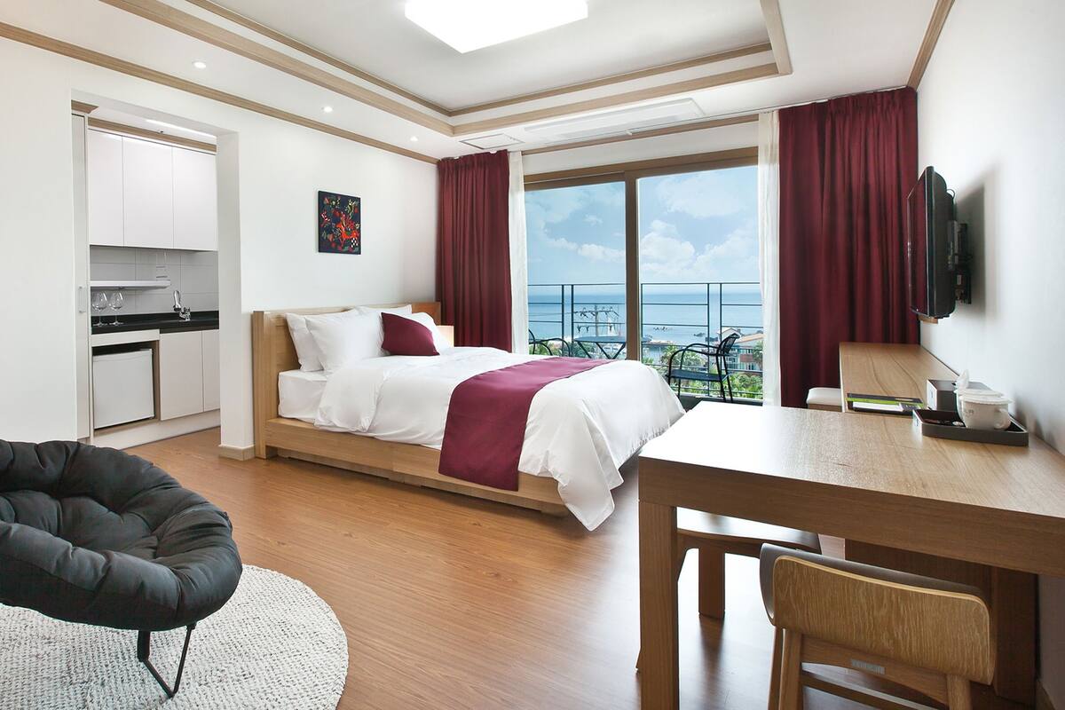 Une chambre d’hôtel moderne équipée d’un lit, d’un bureau, d’une chaise, d’un coin cuisine et d’un balcon avec vue.