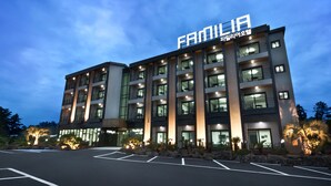A multi-story hotel with a prominent "FAMILIA" sign, featuring a modern architectural design with large windows and a parking lot in front. - Familia Hotel Jeju (Seogwipo)