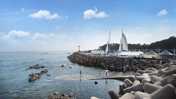A coastal view with a rocky breakwater, a lighthouse, and sailboats. - Familia Hotel Jeju (Seogwipo)