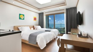 A hotel room with a bed, a desk, a chair, a TV, and a balcony with a view of the sea. - Familia Hotel Jeju (Seogwipo)