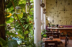 An indoor dining area with tables, chairs, hanging light fixtures, and potted plants. - Hotel Santa Ana (Mérida)