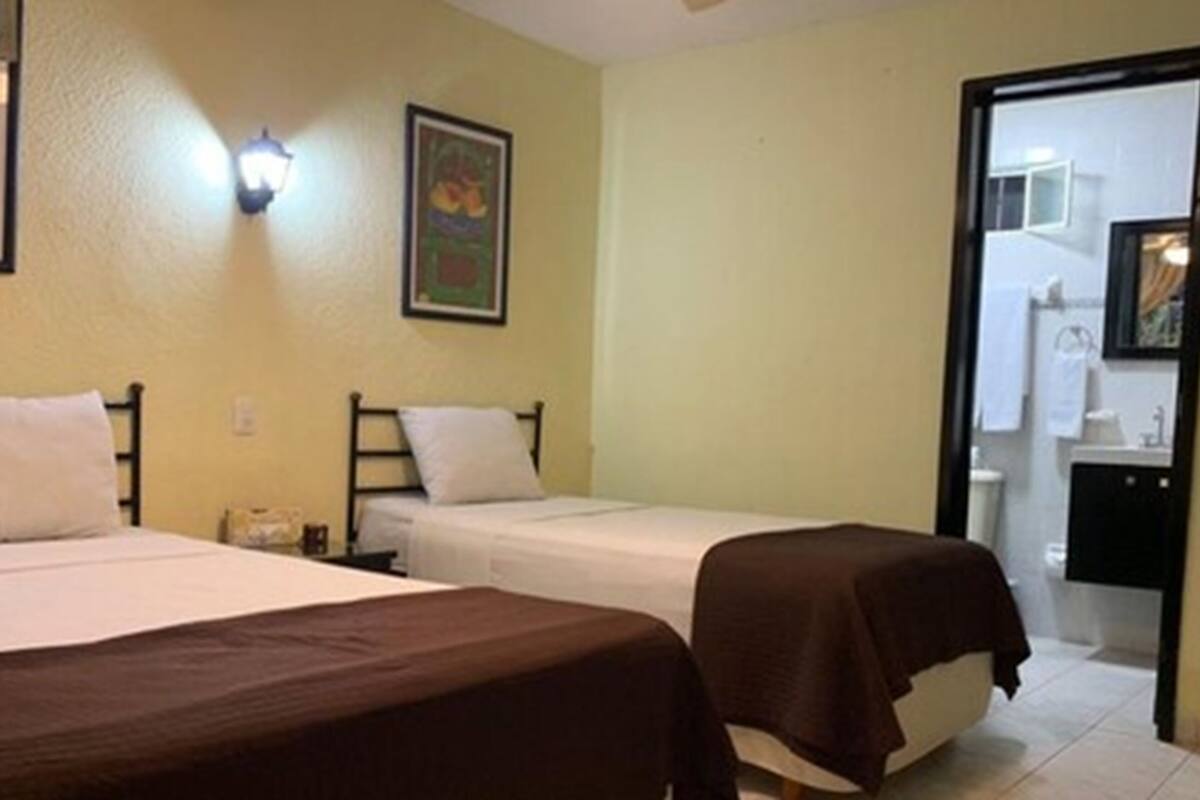 A room with two single beds, a nightstand, a wall-mounted light, and a door leading to a bathroom.
