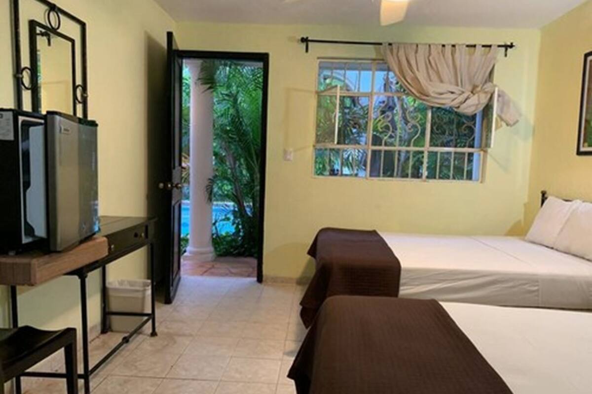 A hotel room with two beds, a desk with a television, and a window with curtains.
