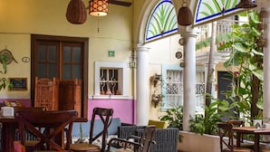 A spacious indoor area with wooden furniture, hanging lamps, and large windows with blue frames. - Hotel Santa Ana (Mérida)