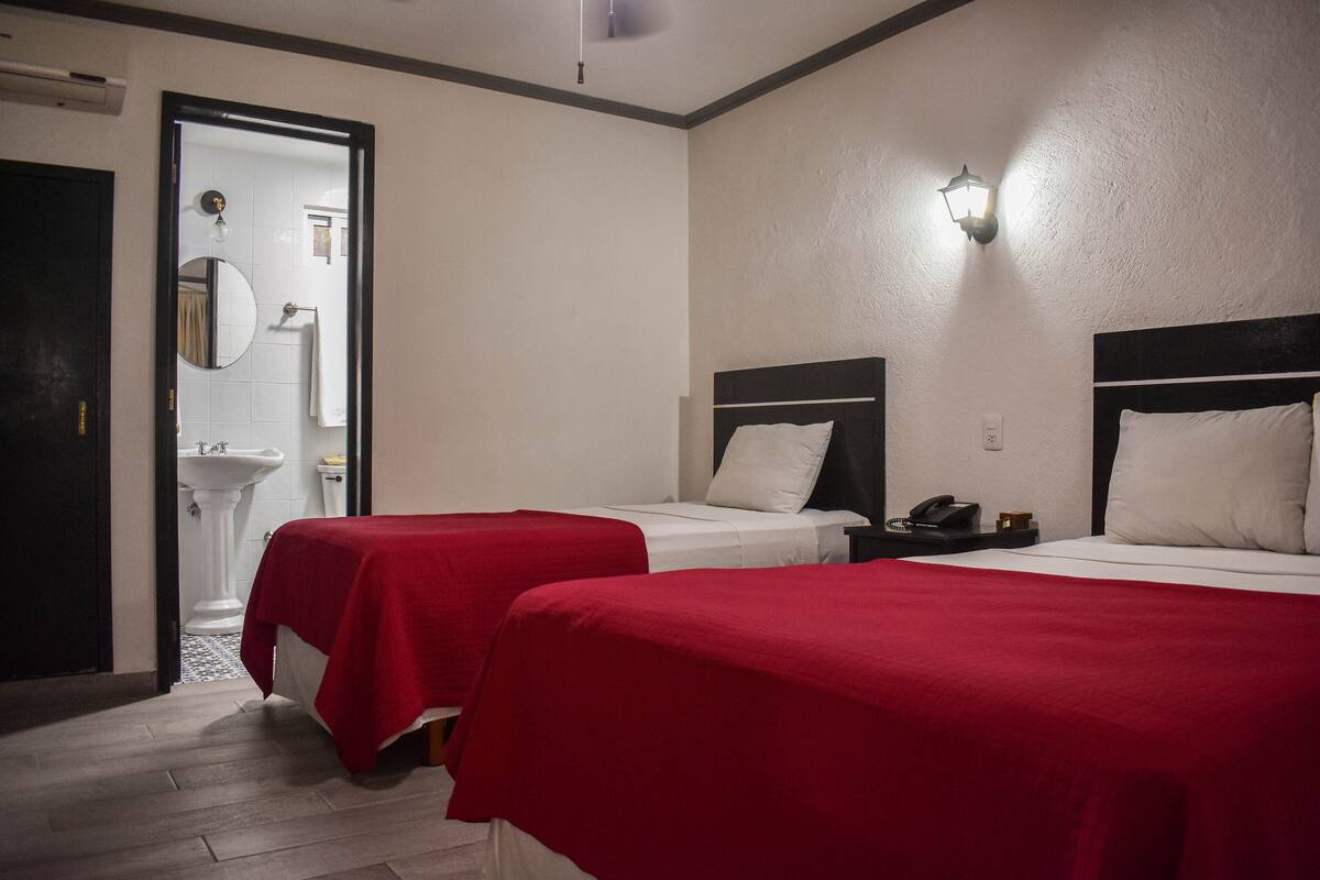 A hotel room with two single beds, a bedside table with a phone, and a mirror on the wall.