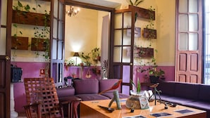 A cozy living room with a wooden coffee table, purple sofas, and various potted plants. - Hotel Santa Ana (Mérida)