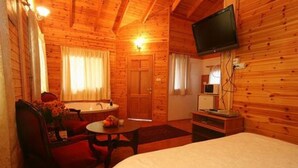 A wooden cabin with a bed, a TV, a small table with fruit, and a chair. - Amirim Atmosphere (Merom HaGalil)