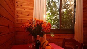 A wooden cabin interior with a dining table set for two, a bottle of wine, and a fruit bowl. - Amirim Atmosphere (Merom HaGalil)