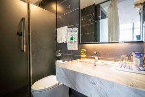 A modern bathroom with a marble sink, a toilet, a glass shower enclosure, and a mirror. - Blue Peninsula Hotel (Xiamen)