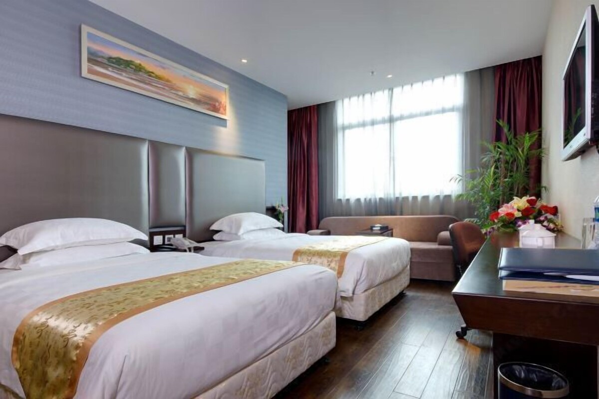 A hotel room with two beds, a sofa, a desk, and a large window with curtains.
