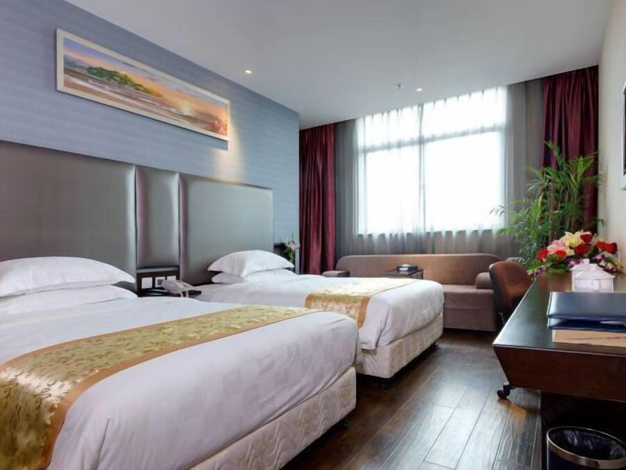 Une chambre d’hôtel avec deux lits, un canapé, un bureau et une grande fenêtre avec des rideaux.