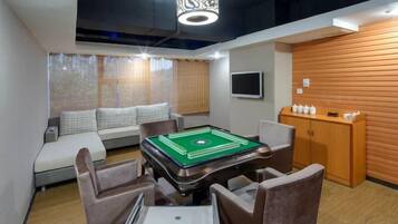 A billiards table with chairs, a sofa, and a television on a wall.