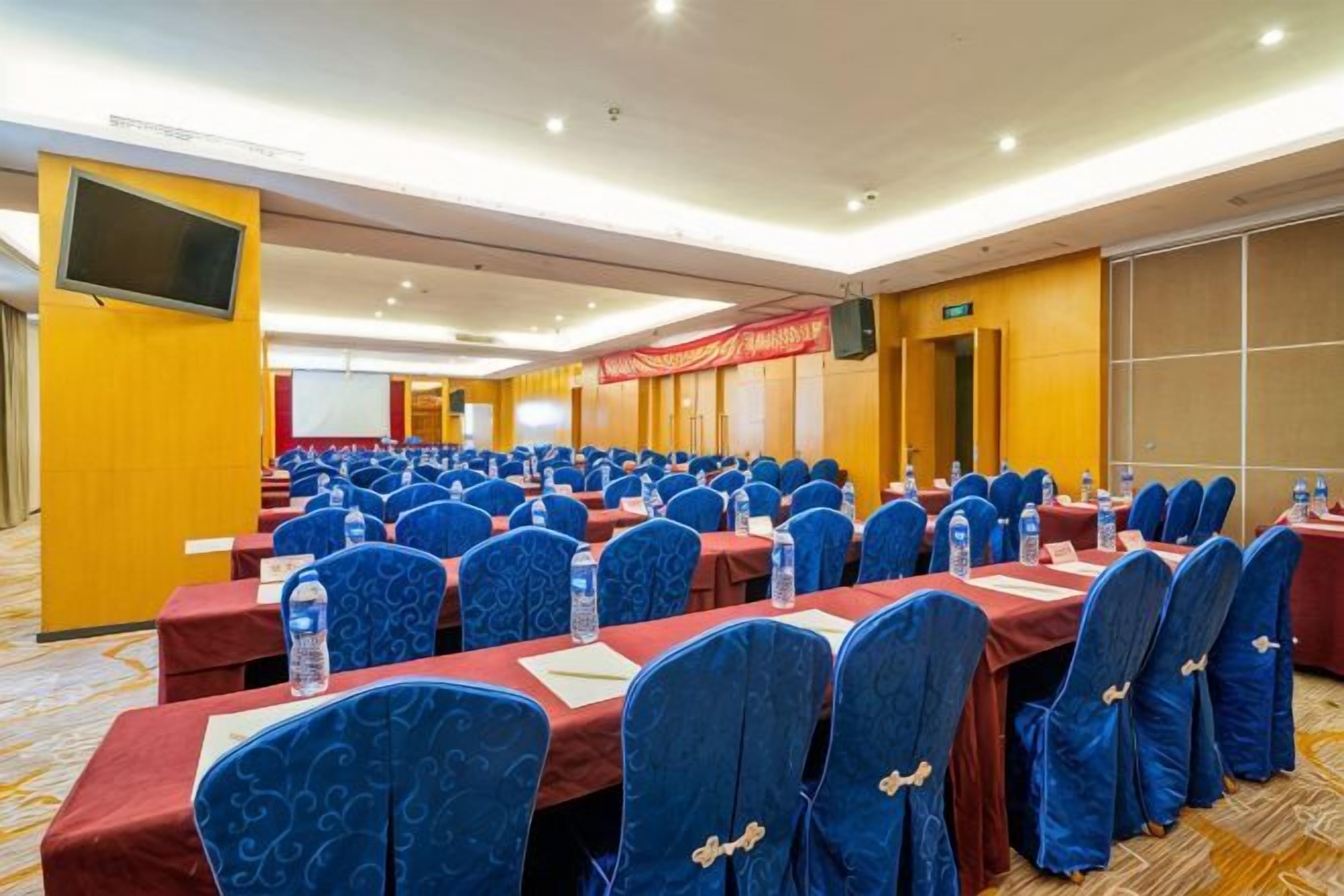 A conference room with rows of tables and chairs, a television screen, and a stage area.