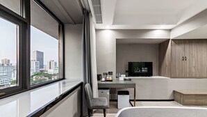 Una habitación de hotel moderna con un gran ventanal, una cama, un escritorio con televisor y un armario.