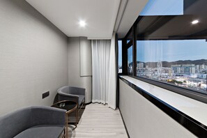 Una habitación de hotel moderna con vistas a la ciudad, un pequeño rincón de descanso y un ventanal grande.