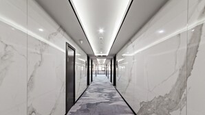 Un pasillo moderno de hotel con paredes de mármol, alfombra estampada e iluminación empotrada.