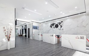 Una moderna zona de recepción de hotel con paredes de mármol, un mapa mundial y una pantalla digital.