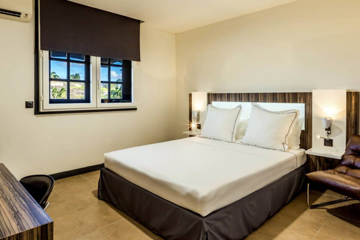 A hotel room with a large bed, a desk, a chair, and a window with a view of greenery.