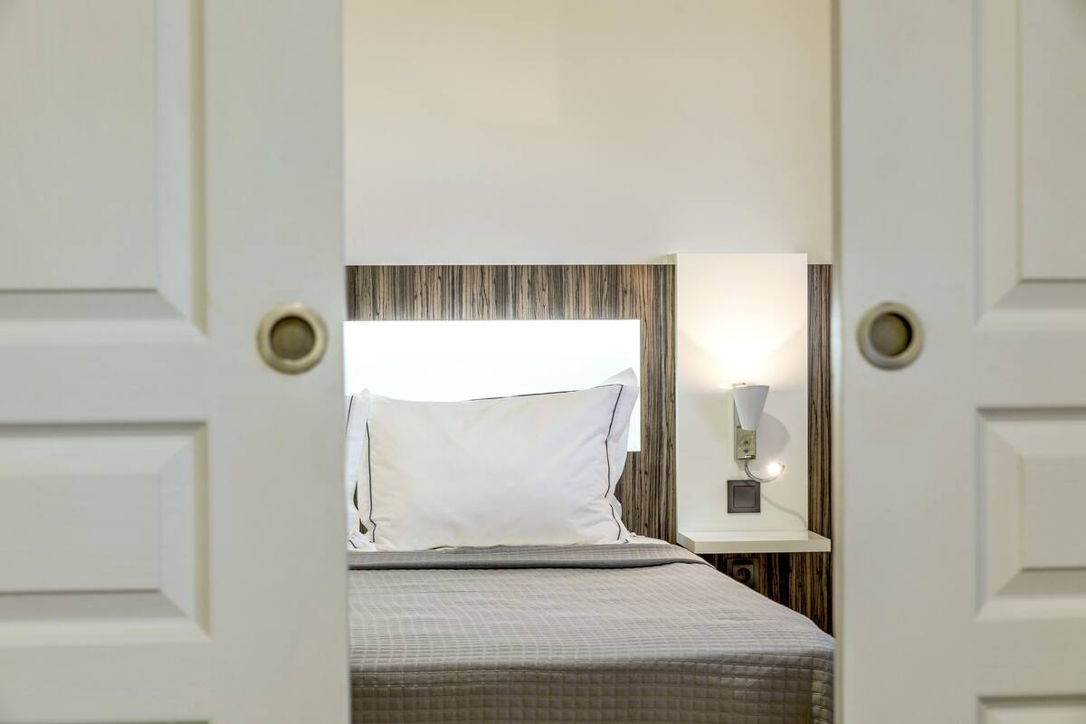 A hotel room with a bed, a nightstand, and a wall-mounted lamp.