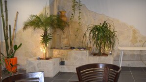 A seating area with wooden chairs and a table, surrounded by potted plants and a stone wall. - Fort Savane (Fort-de-France)
