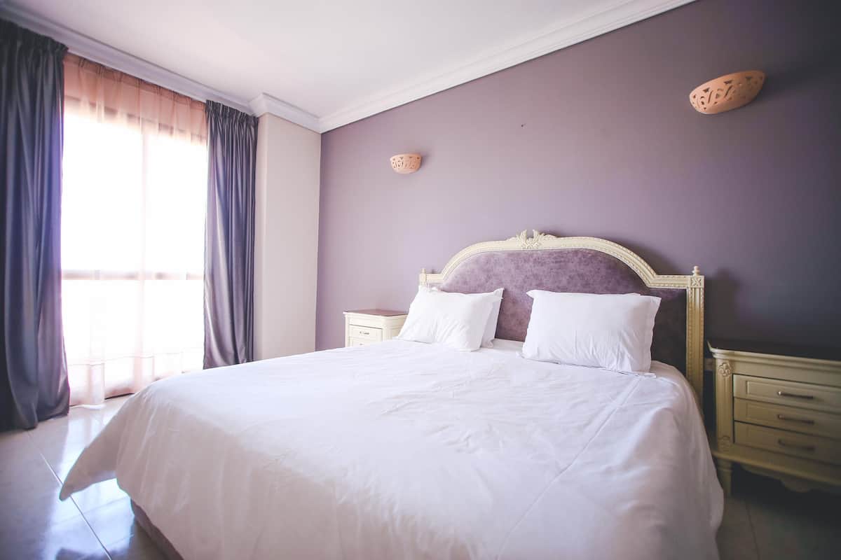 A neatly made bed with white linens, a wooden headboard, and two bedside tables with lamps.