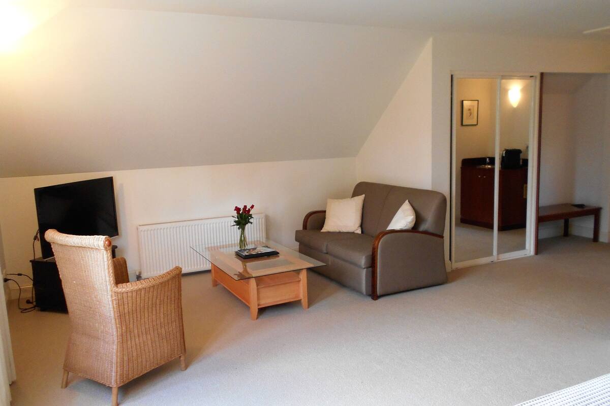 A living room with a sofa, a wicker chair, a coffee table, a flat-screen TV, and a radiator.