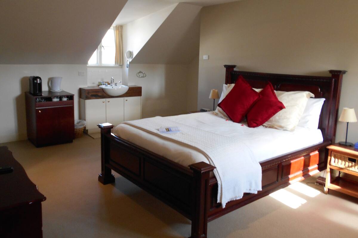 A bedroom with a large bed, a wooden dresser, a sink, and a mirror.