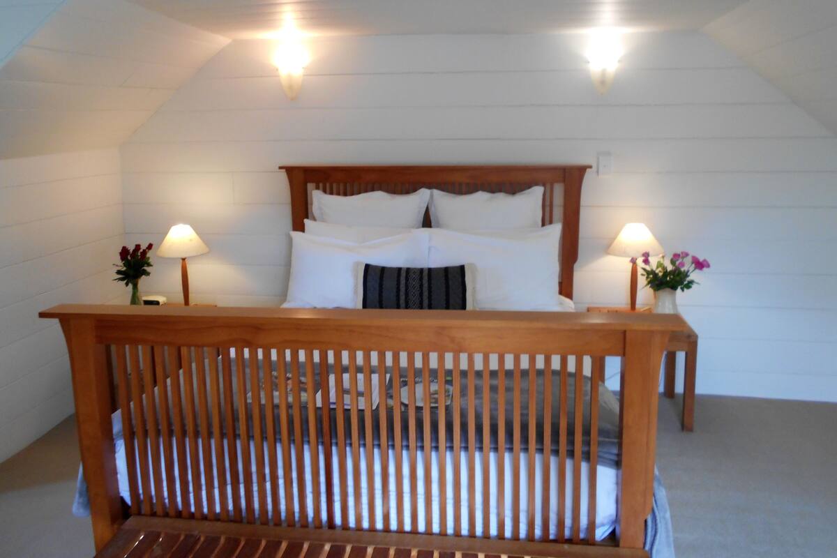 A bedroom with a wooden bed frame, white walls, and two bedside lamps.