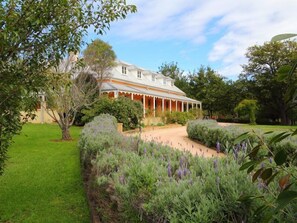 Une grande maison à deux étages, dotée d’un porche et d’un jardin bien entretenu où poussent des plants de lavande.