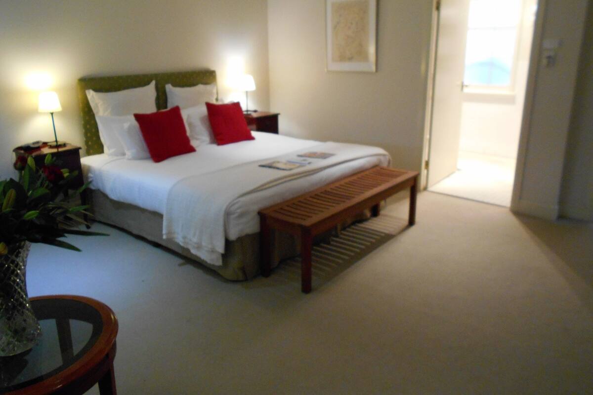 A neatly arranged bedroom with a bed, bedside tables, a bench, and a door leading to another room.