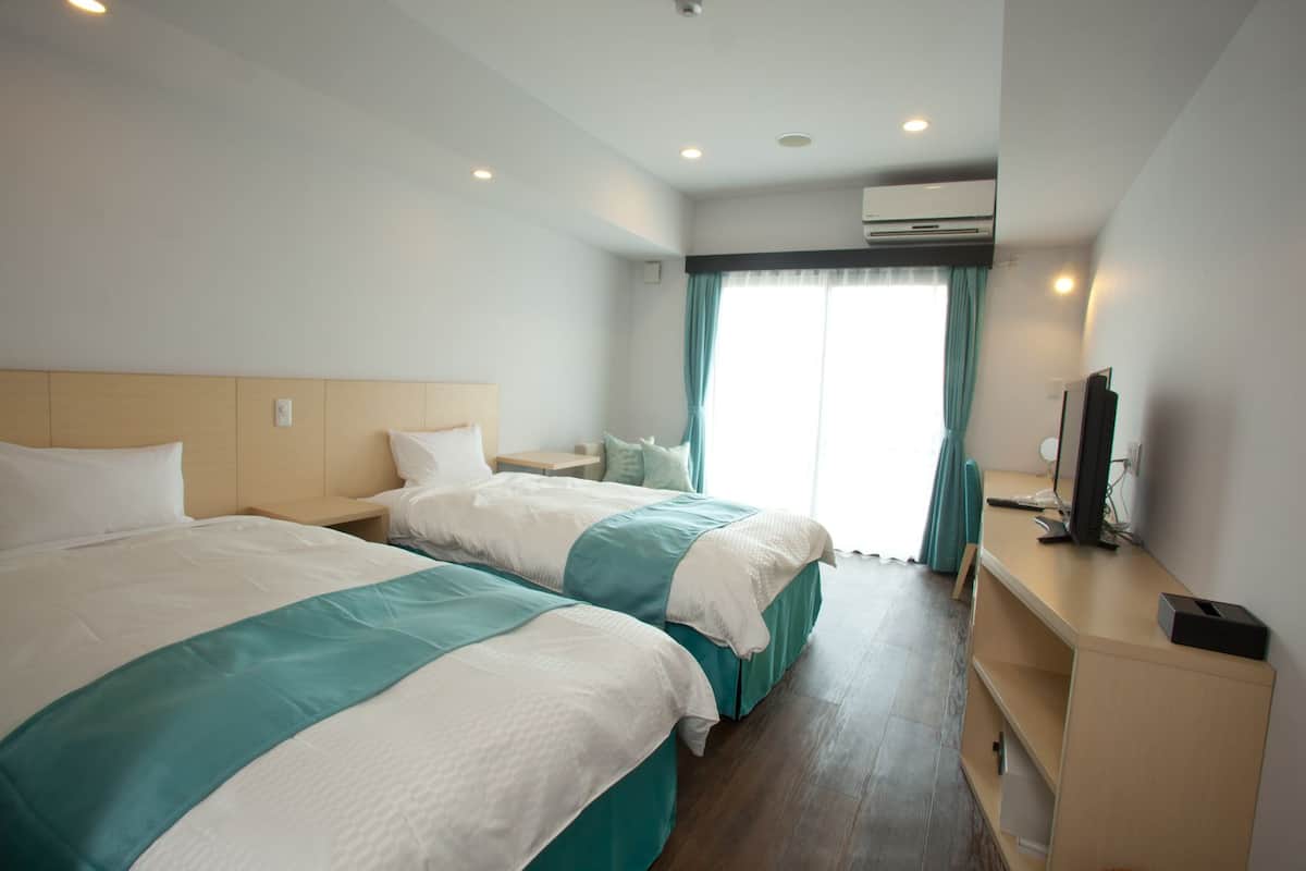 A hotel room with two beds, a desk with a computer, and an air conditioning unit.