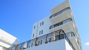 Un hotel moderno con fachada blanca, varios balcones y un muro de acento de piedra.