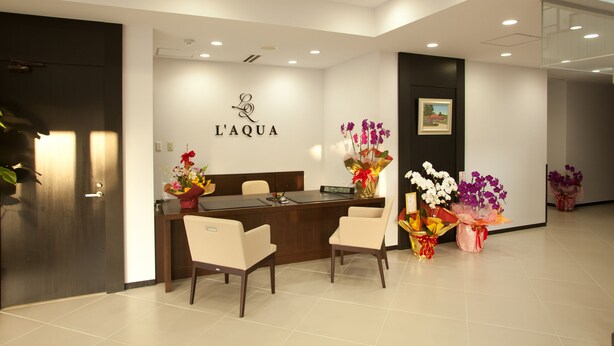 Un área de recepción con un mostrador de madera, dos sillas y un cartel en la pared que dice "L'AQUA".
