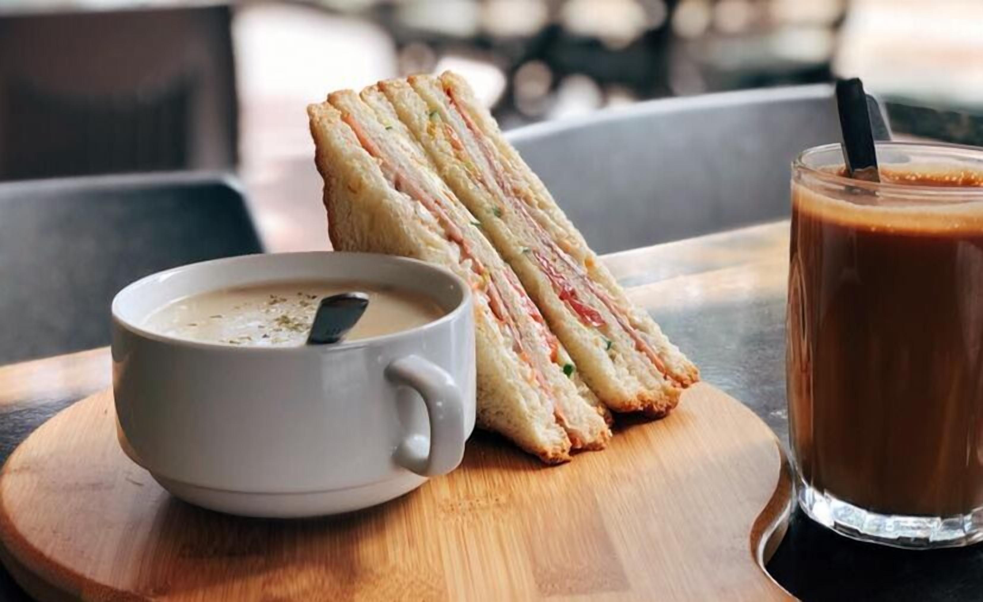 A sandwich, a cup of coffee, and a glass of iced coffee on a wooden table.