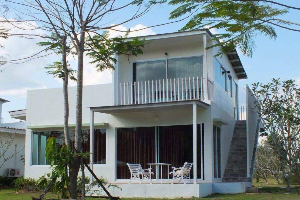 A modern two-story house with a balcony, large windows, and a grassy yard.