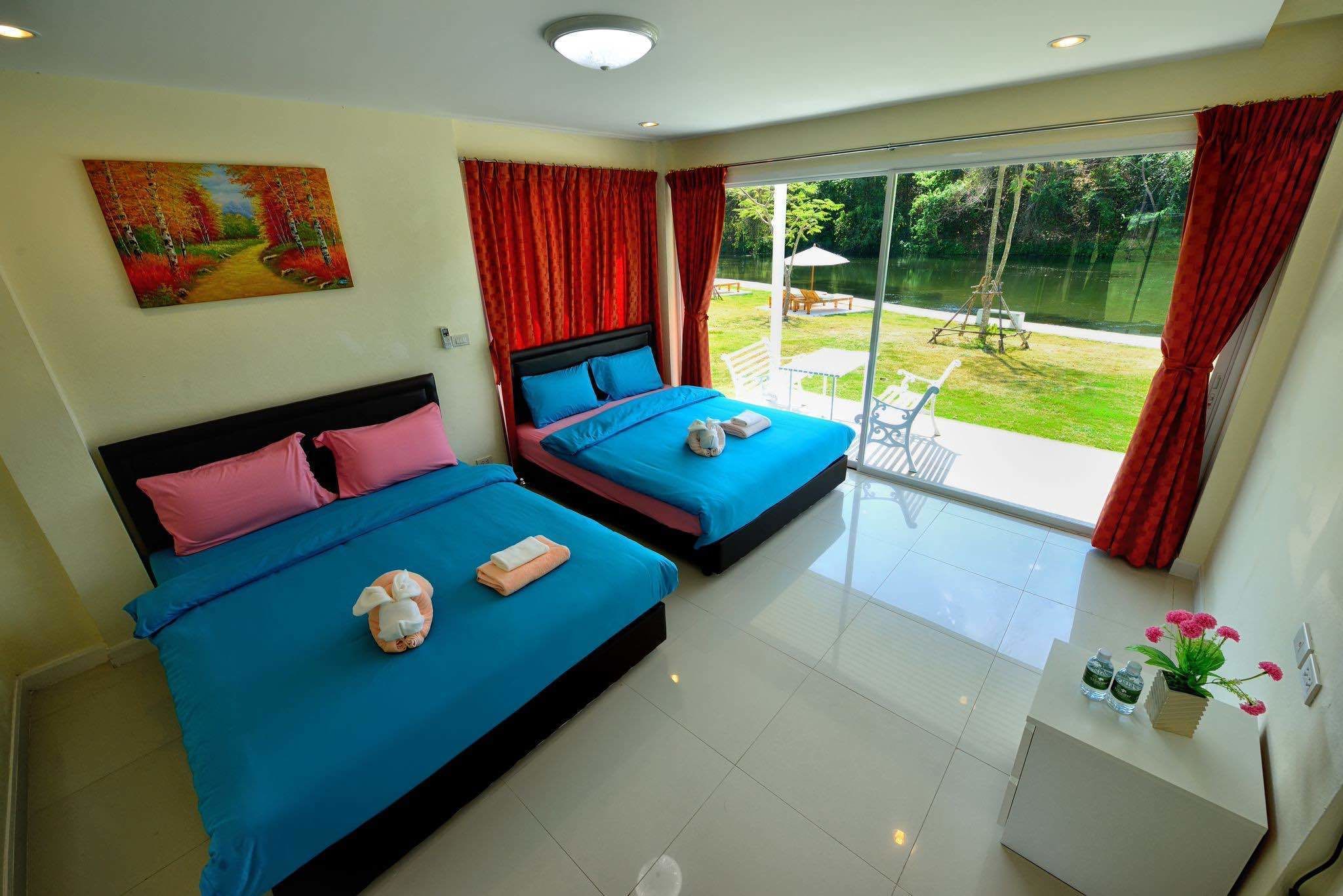 Habitación de hotel con dos camas, un cuadro en la pared y vistas de un jardín a través de amplios ventanales.