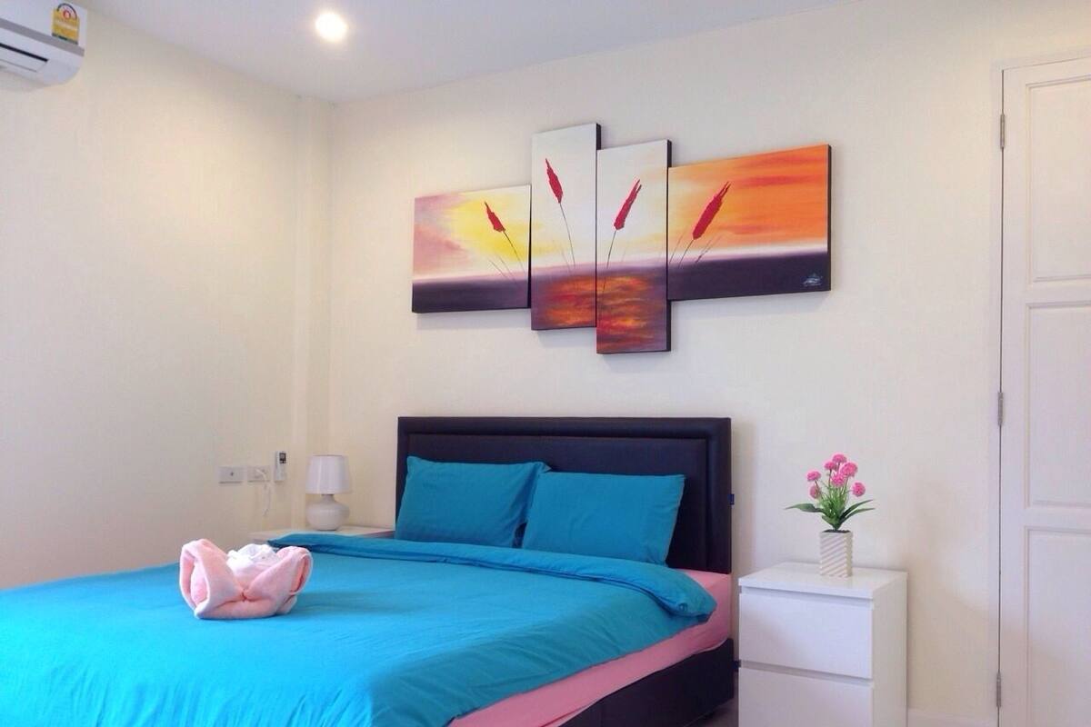 A bedroom with a bed, a nightstand, a wall-mounted air conditioner, and a painting.