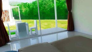 A modern bedroom with a large window, a bed, and a view of a green lawn. - Worawee Resort & Spa (Kaeng Krachan)
