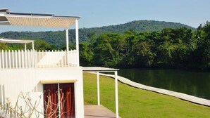 A modern outdoor deck with a white railing, a covered seating area, and a view of a lake and forested hills. - Worawee Resort & Spa (Kaeng Krachan)