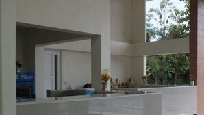 A modern reception area with a glass partition, a reception desk, and a view of tropical vegetation outside. - Worawee Resort & Spa (Kaeng Krachan)