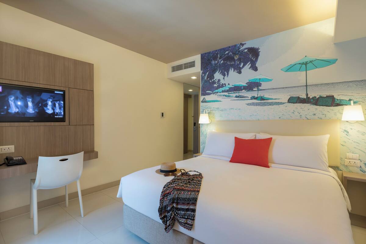 Une chambre d’hôtel avec un lit, un bureau, une télévision et un tableau représentant une scène de plage.