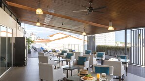 A rooftop dining area with multiple tables and chairs, a ceiling fan, and a view of the cityscape. - Travelodge Pattaya (Pattaya)